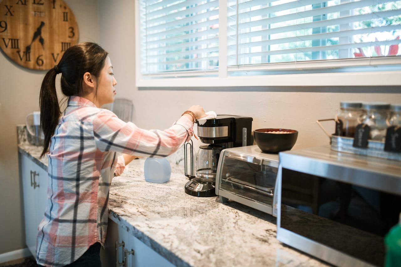services-02 Woman cleaning a coffee maker in a bright, modern kitchen with appliances.
