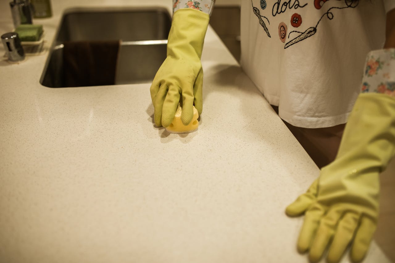 services-01 Woman using yellow rubber gloves to clean a kitchen counter with a sponge.